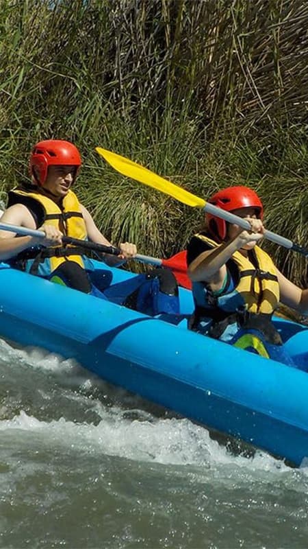 Pareja remando coordinada en un canoaraft neumático superando un rápido en el río Cabriel.