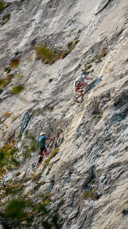 Deportista progresando por los peldaños de una vía ferrata en Venta del Moro con las Hoces del Cabriel de fondo.