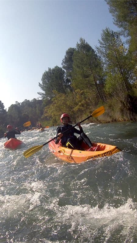 Kayakista navegando en un open kayak individual por las aguas turquesas del río Cabriel entre paredes de roca.