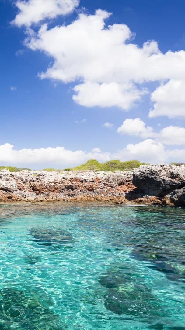 Grupo de personas practicando paddle surf en las aguas turquesas de la costa norte de Menorca cerca de un acantilado.