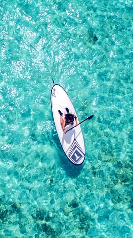Grupo de personas practicando paddle surf en las aguas turquesas de la costa norte de Menorca cerca de un acantilado.
