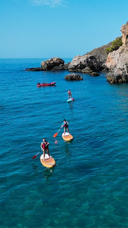 Persona practicando paddle surf frente a la Cascada de Maro en los acantilados de Nerja.
