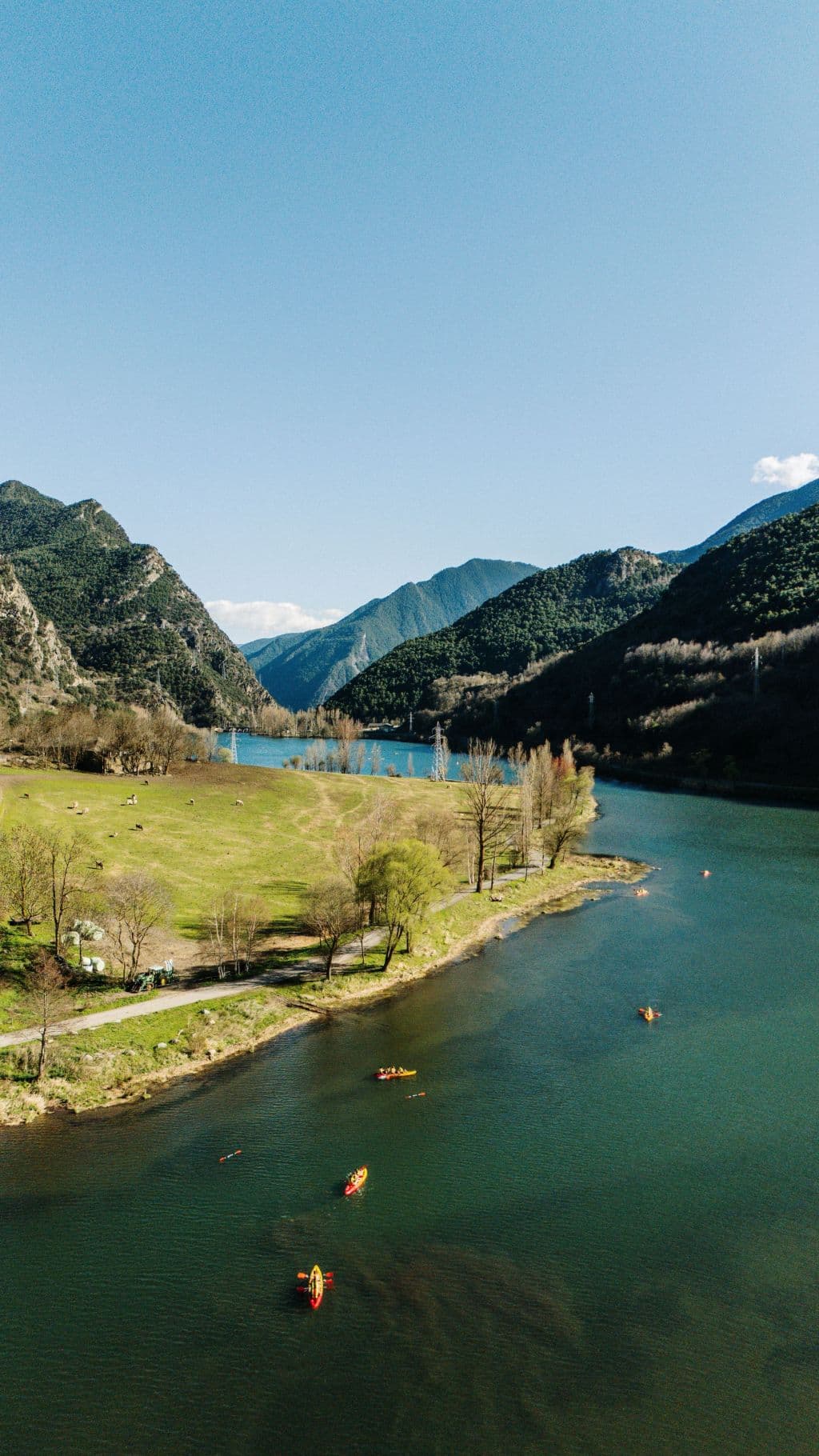 Varias personas navegando en kayaks individuales y dobles por las aguas tranquilas del lago de La Torrassa, rodeados de vegetación.