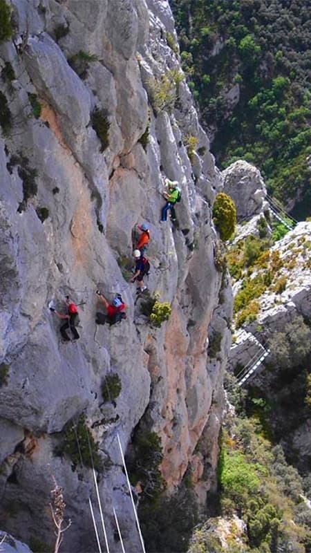 Aventurero cruzando un puente tibetano en la Vía Ferrata Croqueta d'Obarra con el paisaje pirenaico de fondo.